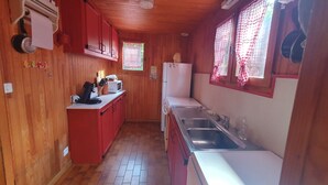 Une cuisine compacte aux murs en bois et au plan de travail rouge. Elle comprend un évier, un four à micro-ondes et un réfrigérateur.