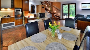 Una cocina moderna con armarios de madera, horno empotrado y microondas. Hay un comedor con mesa y sillas de madera, y un jarrón con flores.