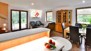 Una cocina moderna con encimera blanca, comedor con mesa y sillas de madera, y vistas al exterior con vegetación.