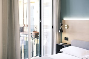 Een hotelkamer met een bed, een nachtkastje, een wandlamp en uitzicht op een balkon met een leuning en een bloempot.