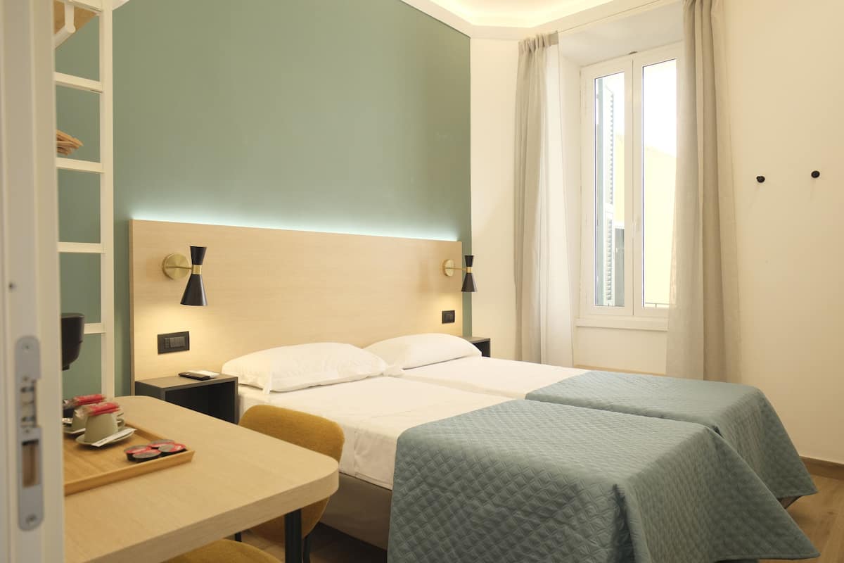 Une chambre d’hôtel avec un lit, des tables de chevet, un bureau et une fenêtre avec des rideaux.