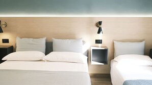 Ein Hotelzimmer mit zwei Betten, jeweils mit weißer Bettwäsche und Kissen. An den Nachttischen stehen Lampen, und über den Betten ist eine Wandleuchte angebracht.