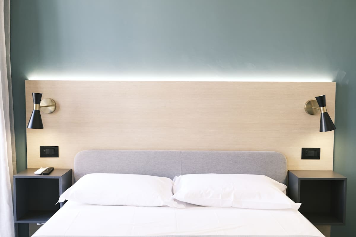 Un lit bien fait, avec du linge de lit blanc, deux tables de chevet avec des lampes noires et une tête de lit de couleur claire.