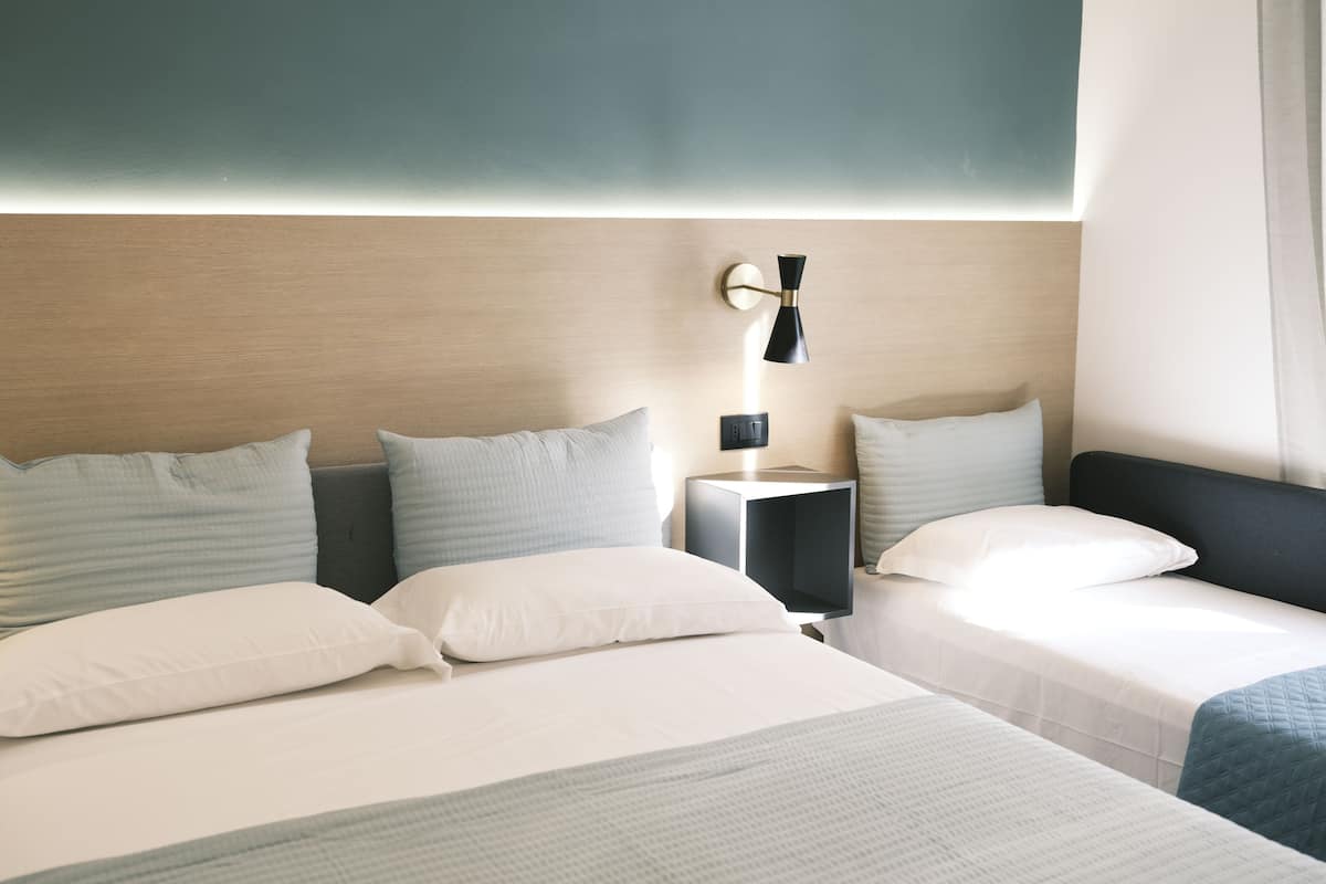 Une chambre d’hôtel avec deux lits, une table de chevet avec une lampe et une tête de lit dotée d’un panneau lumineux.