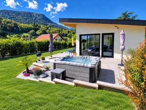 Una casa moderna con jacuzzi, mobiliario exterior y vistas a la montaña.
