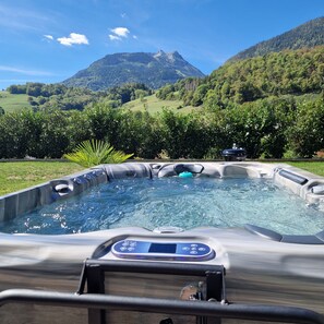 A hot tub with a control panel, surrounded by lush greenery and mountains in the background.