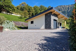 Une maison moderne avec une façade en pierre, une allée en gravier et une vue sur les montagnes en arrière-plan.