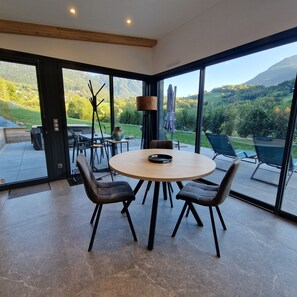 Un espace repas moderne avec une table ronde, quatre chaises et une vue sur un paysage montagneux grâce à de grandes fenêtres.