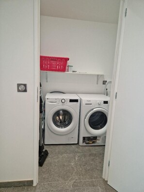 Une buanderie avec deux machines à laver et un panier rouge posé sur une étagère.