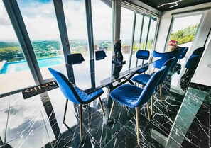 A dining area with a glass table and blue chairs, overlooking a pool and landscape. - 𝗟𝗮 𝗖𝗮𝘀𝗶𝘁𝗮 𝗡𝗲𝗴𝗿𝗮 𝗲𝗻 𝗖𝗮𝘆𝗲𝘆

 (Barrio Beatriz)