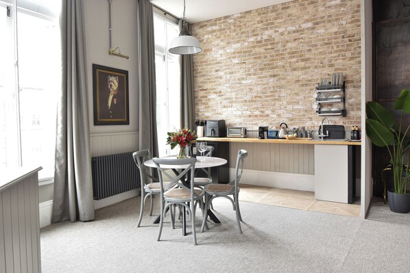 A modern kitchen with a brick wall, a dining area with a round table and chairs, and a potted plant.