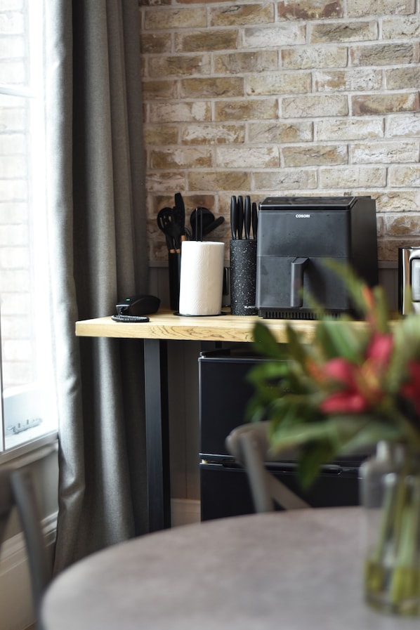 A kitchen area with a brick wall, a wooden countertop, a coffee machine, a phone, and a vase with flowers. - Yorkshire Grey Pub & Rooms (London)