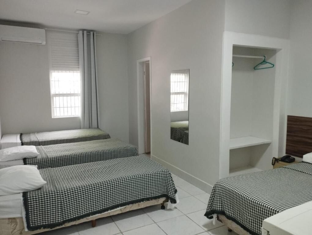 Quarto com três camas de solteiro, um espelho, um cabideiro e uma pequena prateleira.