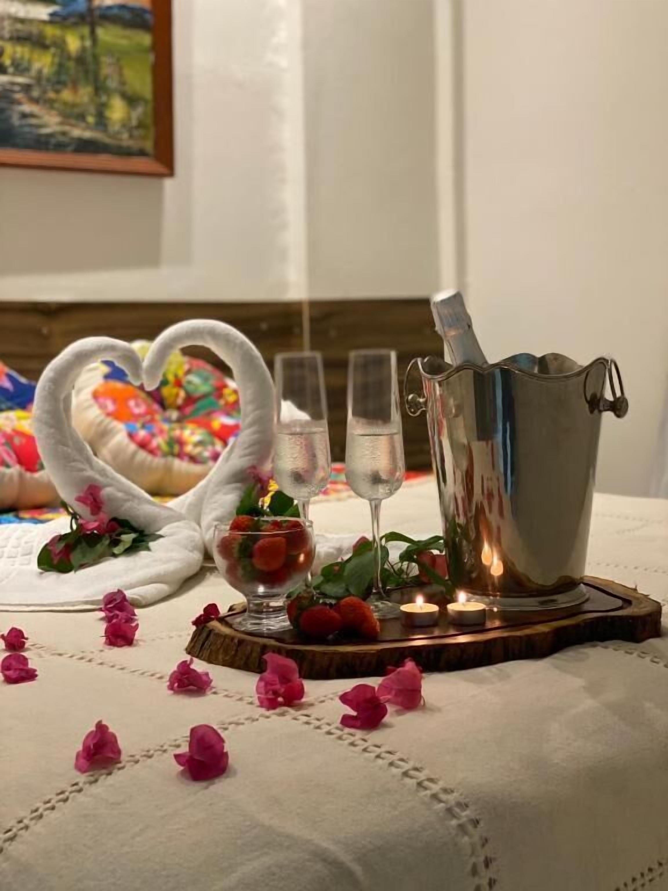 Una habitación acogedora con una cama, una toalla con forma de corazón, un jarro de plata y vasos de agua sobre una bandeja de madera.