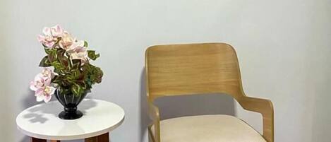 A room with a wooden chair and a small table with a vase of flowers.