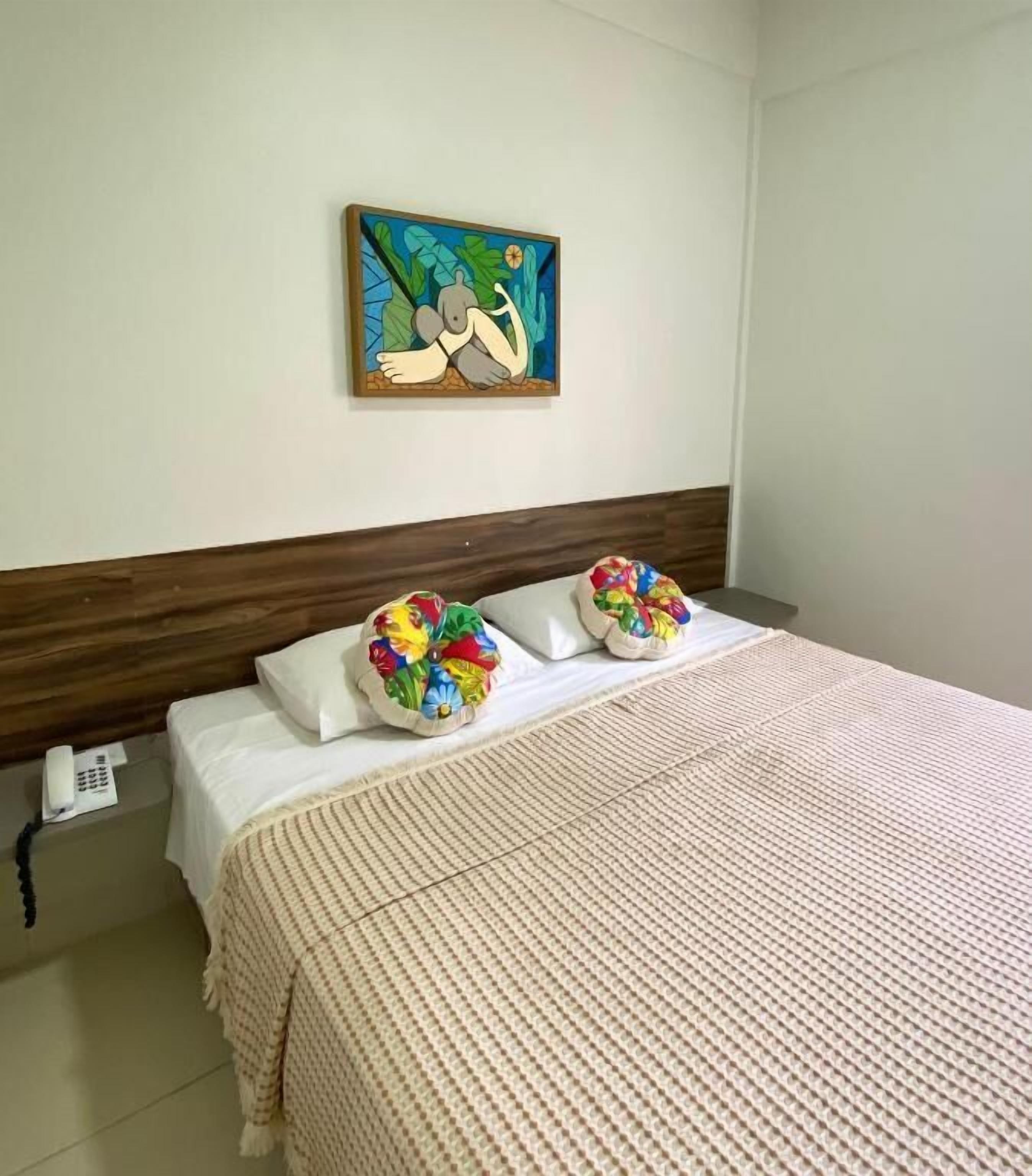 A hotel room with a bed, a headboard, a wall-mounted painting, and a telephone on the nightstand.
