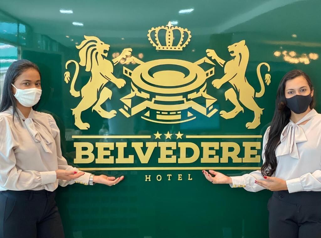 Twee personen staan voor een hotelschild met een leeuwenembleem en kroon, wat wijst op een luxe of koninklijk thema.