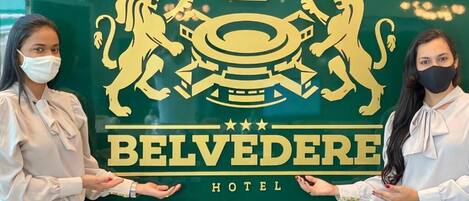 Twee personen staan voor een hotelschild met een leeuwenembleem en kroon, wat wijst op een luxe of koninklijk thema.