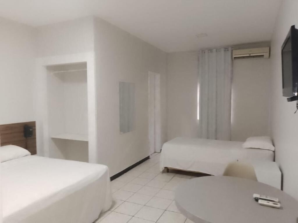 A hotel room with two beds, a round table, a TV, and an air conditioning unit.