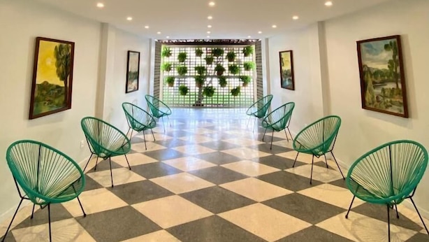 Un hall d’hôtel avec un sol à carreaux, des chaises vertes et des œuvres d’art accrochées aux murs.