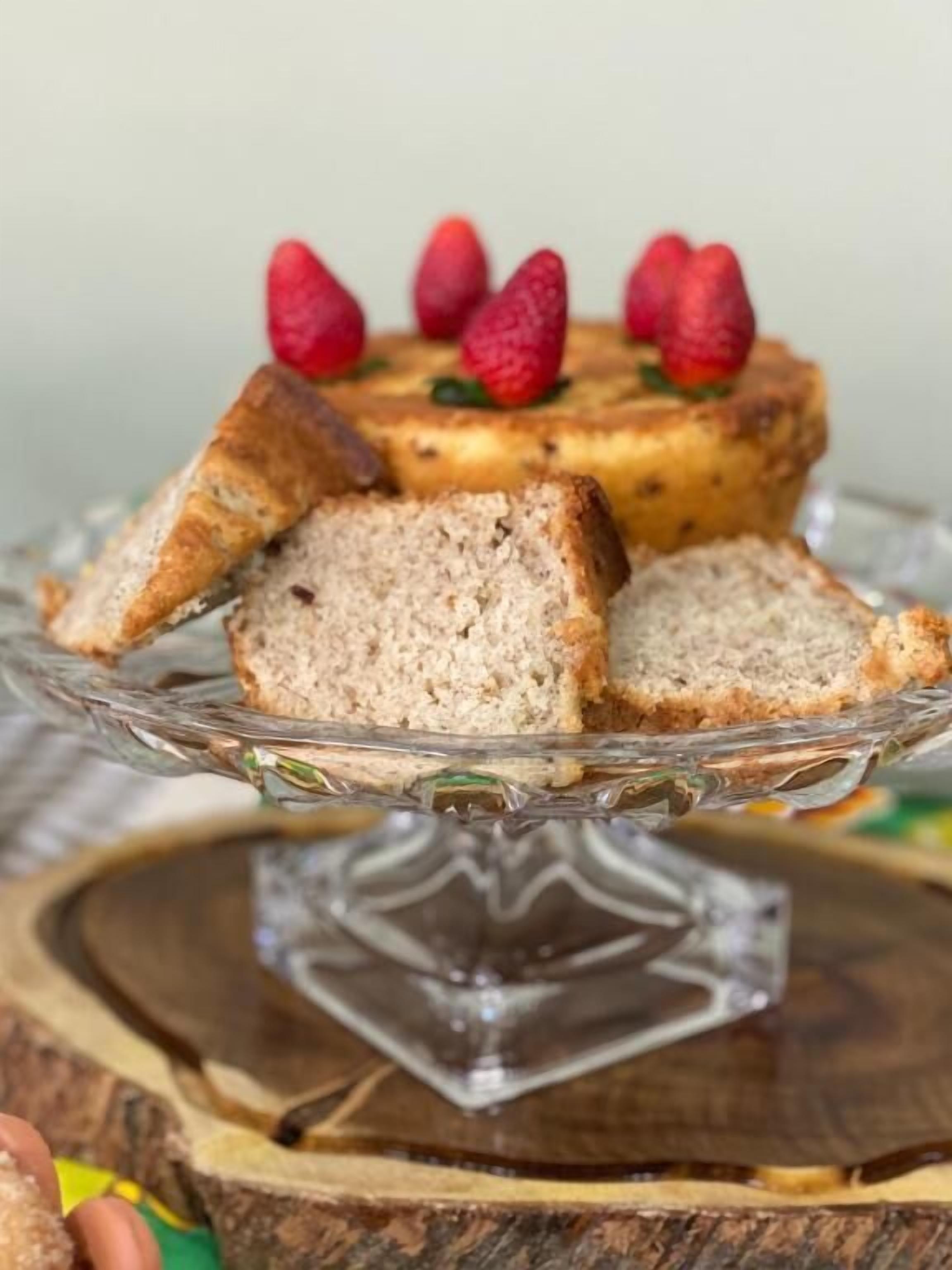 Un pastel con fresas encima, sobre un pedestal de vidrio.