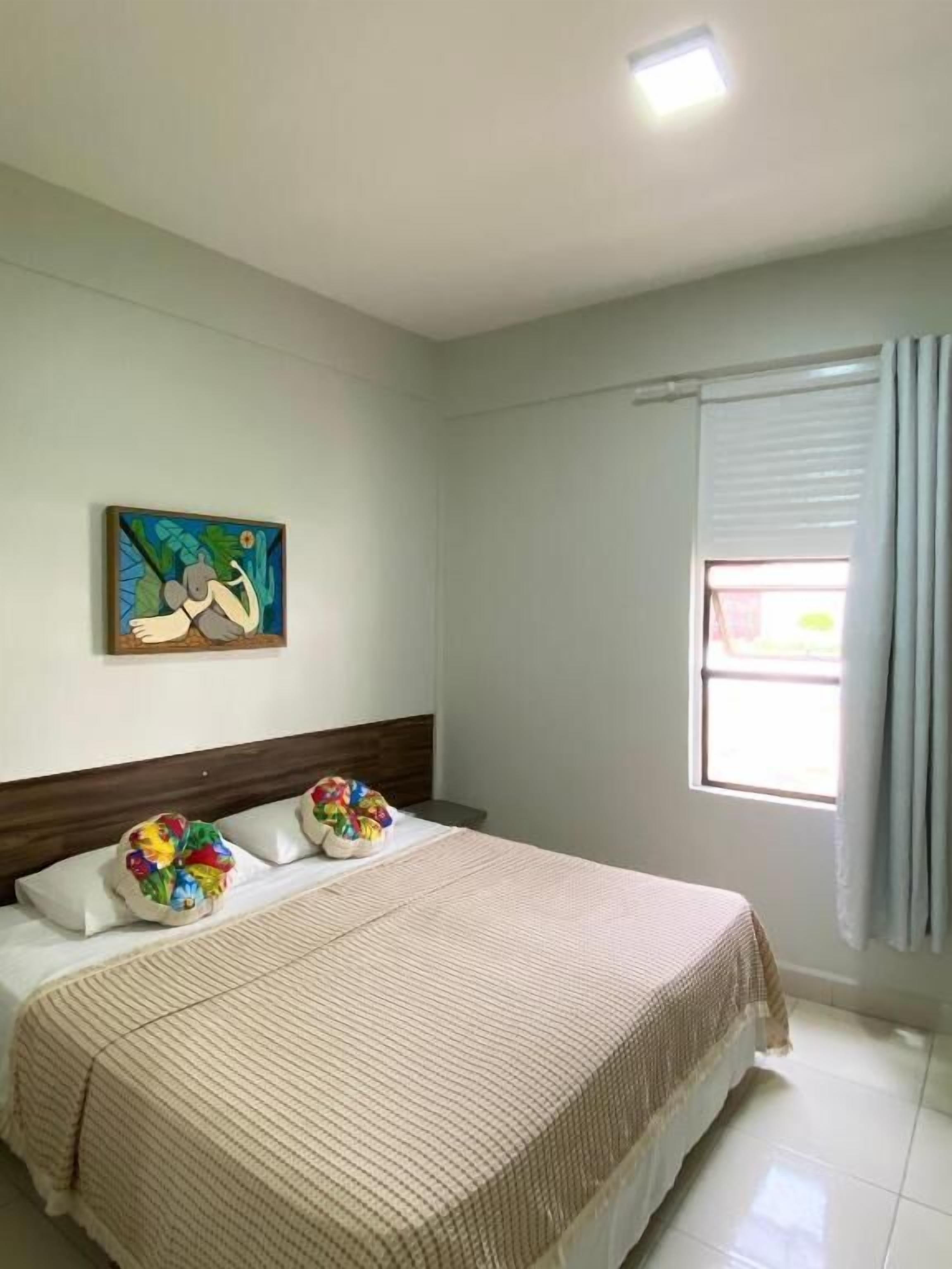 A bedroom with a bed, pillows, a painting, and a window with curtains.