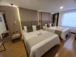 Habitación de hotel con dos camas, una mesita de noche, un pequeño rincón de descanso y un ventanal grande.