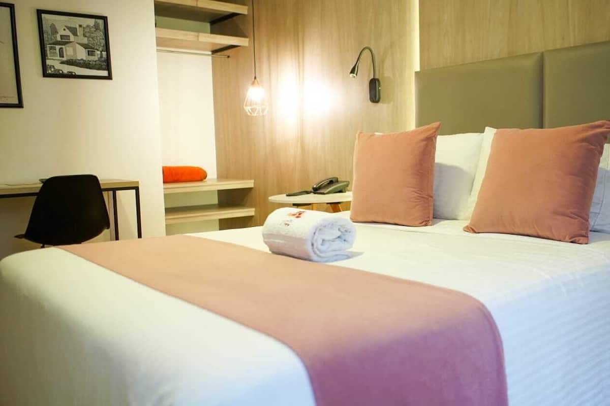 Une chambre d’hôtel avec un lit, un bureau, une chaise, un téléphone et une lampe.