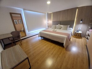 Una habitación de hotel moderna con una cama grande, un escritorio, una silla y una mesita con un teléfono.