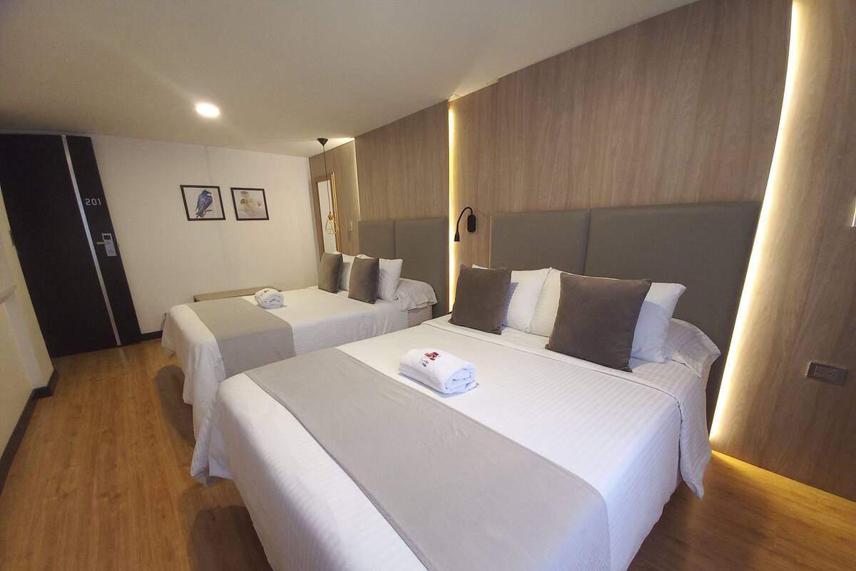 Une chambre d’hôtel avec deux lits, un plancher en bois, un luminaire fixé au mur et une porte portant un numéro.