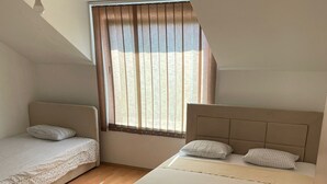 Une chambre avec deux lits, une fenêtre avec des rideaux, un ventilateur de plafond et un plancher en bois.