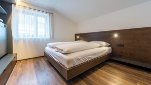 Ein modernes Schlafzimmer mit einem Holzkopfteil, einem Bett mit weißen Leinen, einer Bank und einem Fenster mit durchsichtigen Vorhängen.