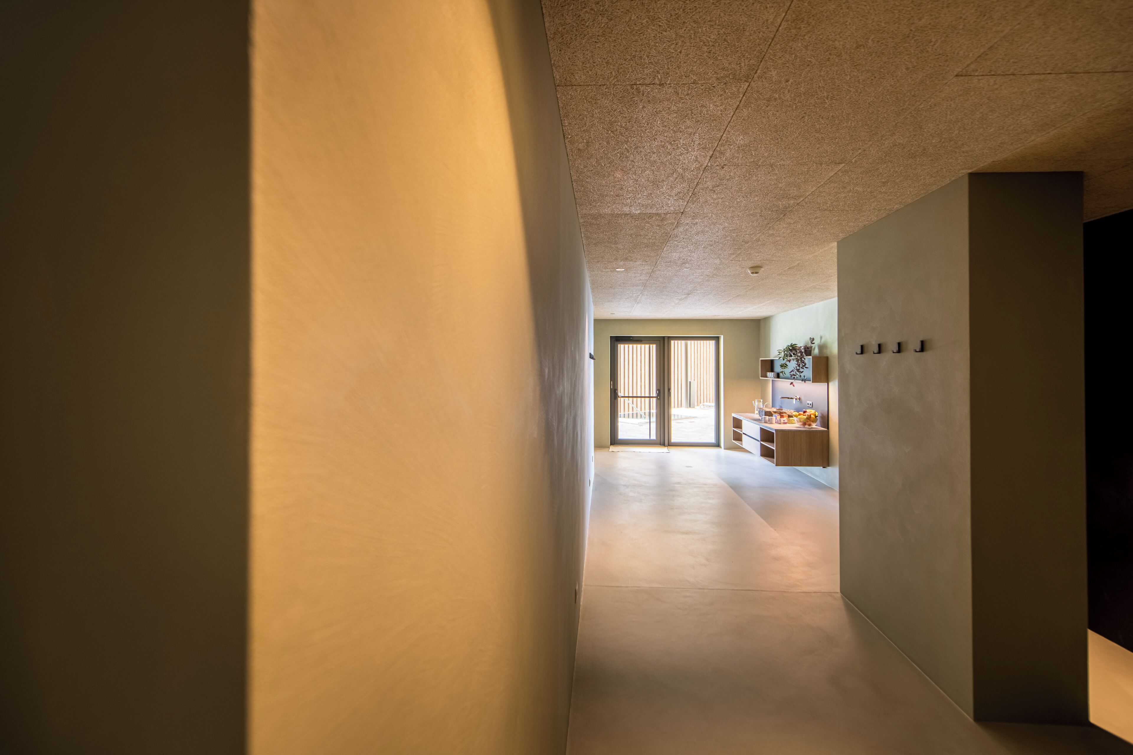 Un pasillo que conduce a una habitación con un ventanal grande, una puerta y una zona de kitchenette.