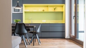 Eine moderne Küche mit einem gelben Regal, einer Mikrowelle, einem Spülbecken und einem Essbereich mit grauem Sofa und schwarzen Stühlen.