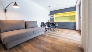 Ein modernes Wohnzimmer mit grauem Sofa, Holzboden und einem Essbereich mit einer gelben Kücheninsel.