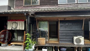 Un edificio tradicional de madera con un porche delantero, puertas correderas de vidrio y un pequeño espacio al aire libre para sentarse.
