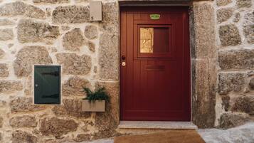 A stone building with a red door, a mailbox, and a small plant on the wall.