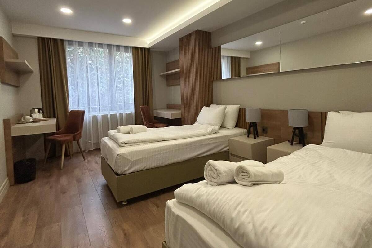 Une chambre d’hôtel avec deux lits, un bureau, une chaise et une grande fenêtre avec des rideaux.