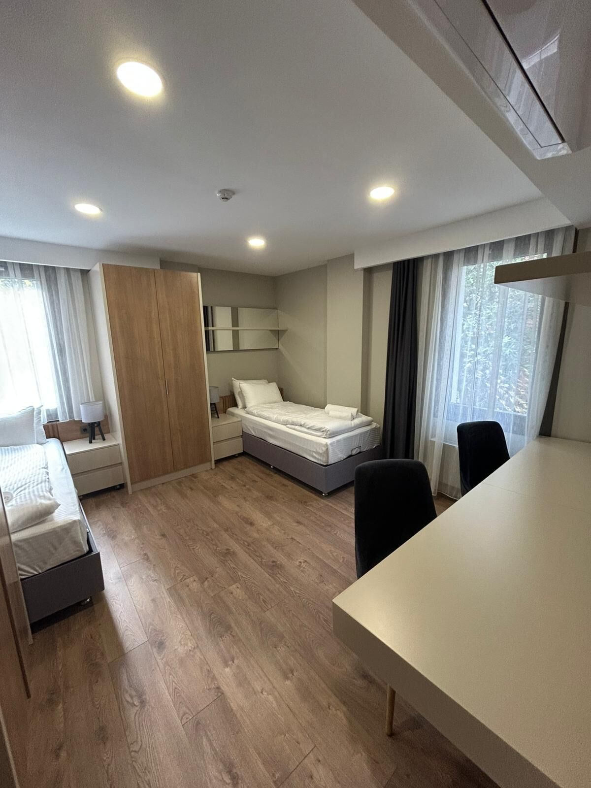 Una habitación moderna y luminosa con una cama, una mesita de noche y una mesa de comedor con sillas.
