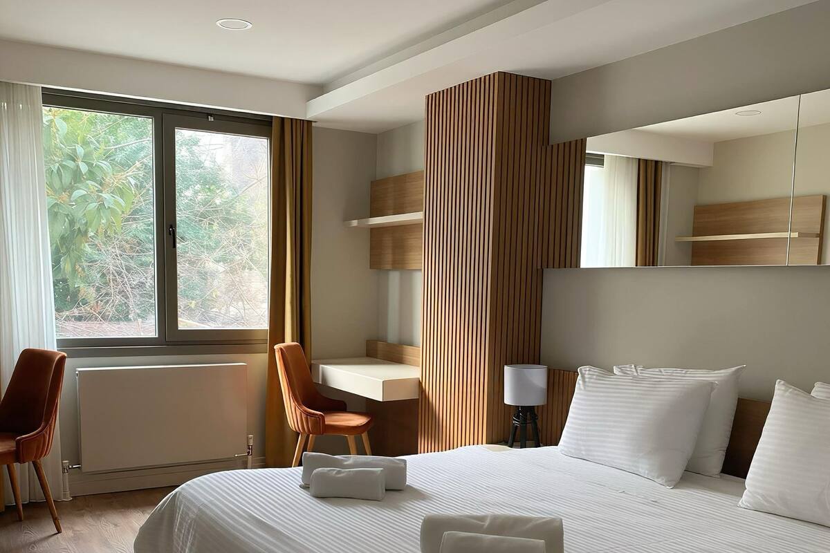 Une chambre d’hôtel moderne, dotée d’un grand lit, d’un bureau, d’une chaise et d’une fenêtre donnant sur la verdure.