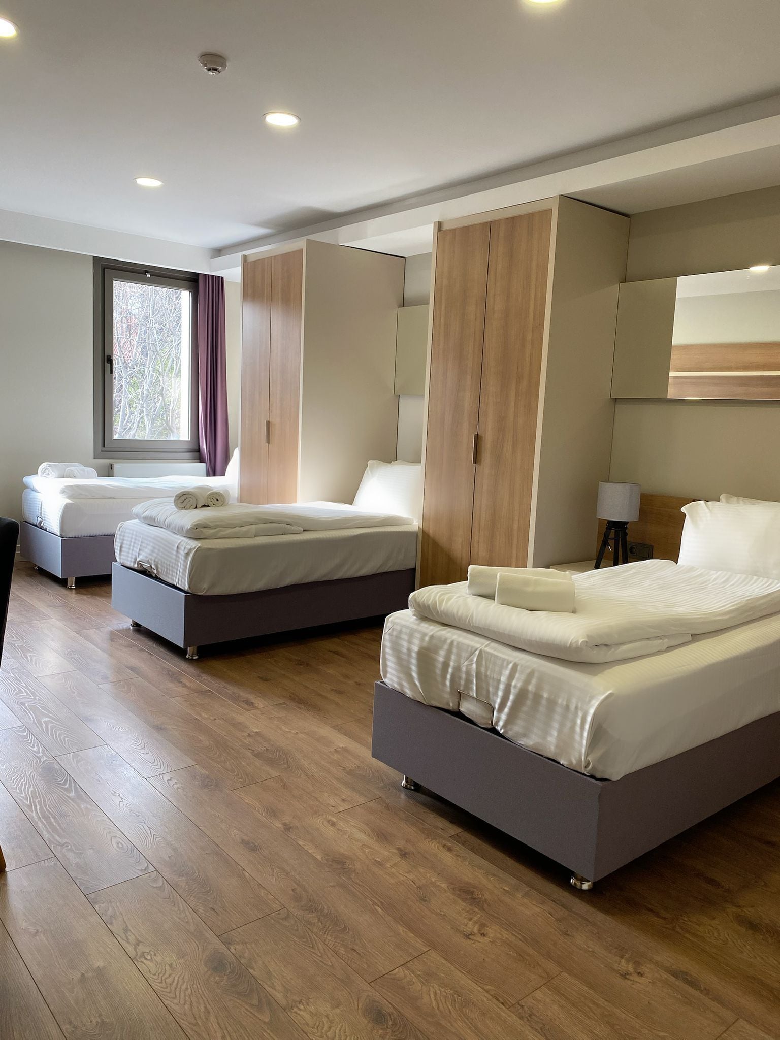 Una habitación de hotel moderna con dos camas, suelo de madera y un ventanal con cortinas.