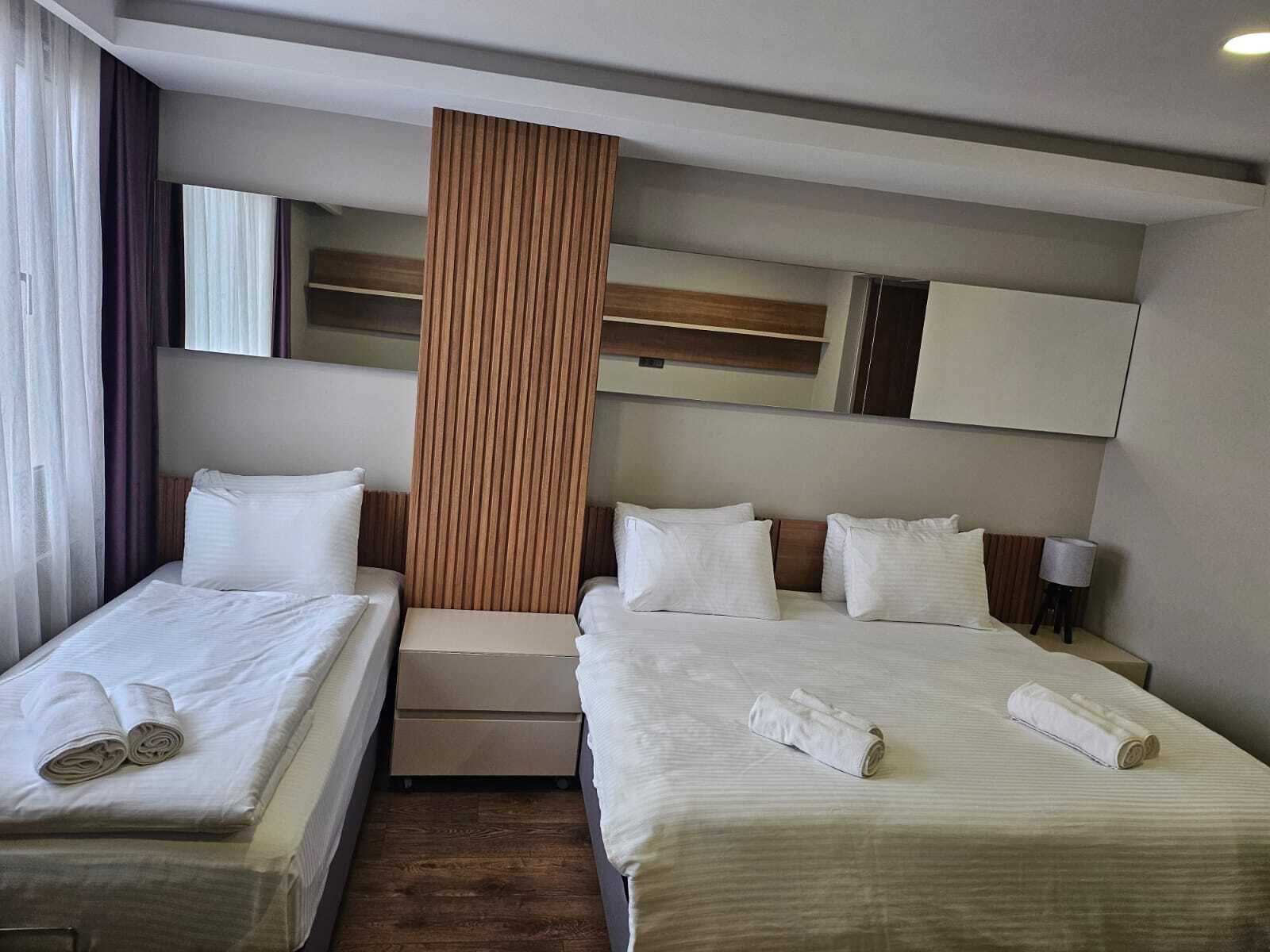 A hotel room with two beds, a wooden accent wall, a mirror, and a bedside table with a lamp.