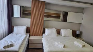 A hotel room with two beds, a wooden accent wall, a mirror, and a bedside table with a lamp.