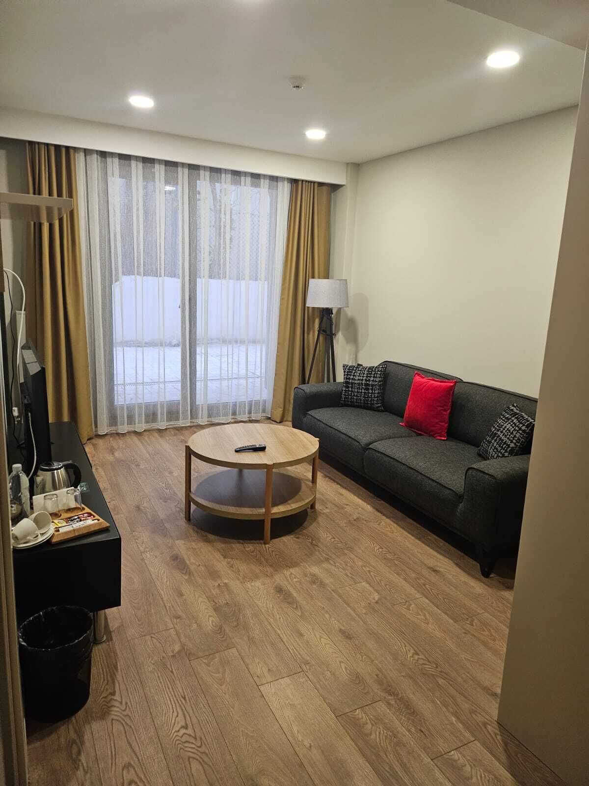 Sala de estar com sofá, mesa de centro, luminária e vista através de amplas janelas.