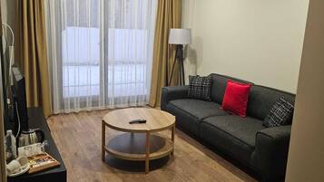 Sala de estar com sofá, mesa de centro, luminária e vista através de amplas janelas.