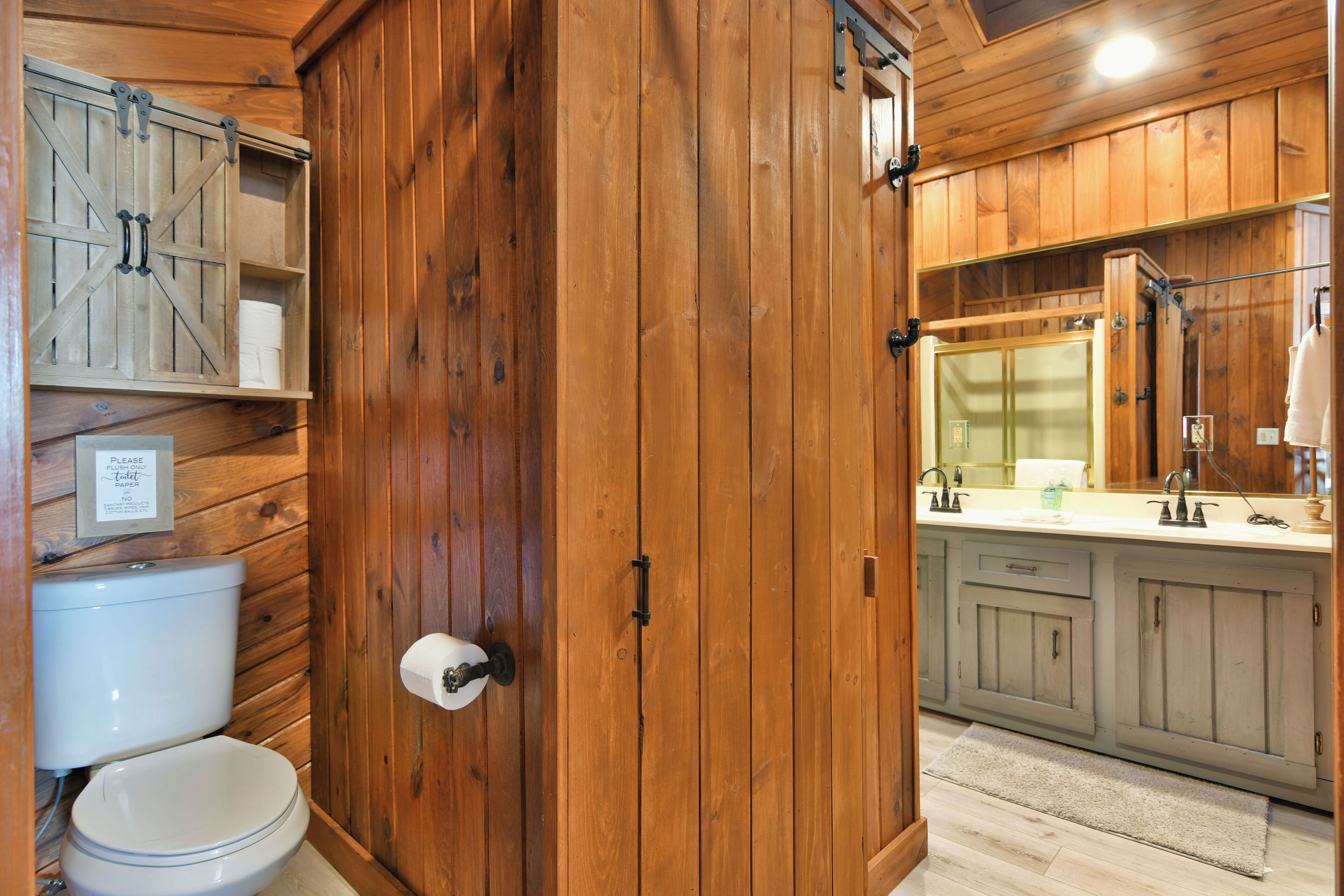 Une salle de bain en bois comprenant des toilettes, un lavabo avec un miroir et un meuble avec une porte de style rustique.