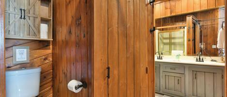 Une salle de bain en bois comprenant des toilettes, un lavabo avec un miroir et un meuble avec une porte de style rustique.