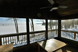 A wooden deck with a table and benches, overlooking a snowy landscape and a body of water. - Spruce Haven (Hayward)