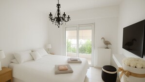 A bedroom with a large bed, a chandelier, a television, and a window with a view of greenery. - Modern Lux Apt by Acropolis I Private Parking, Gym, Balcony, Metro 1-min Walk (Athina)
