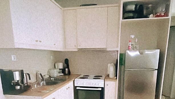 Une cuisine de taille réduite, avec des meubles blancs, une cuisinière, un réfrigérateur et une machine à café.